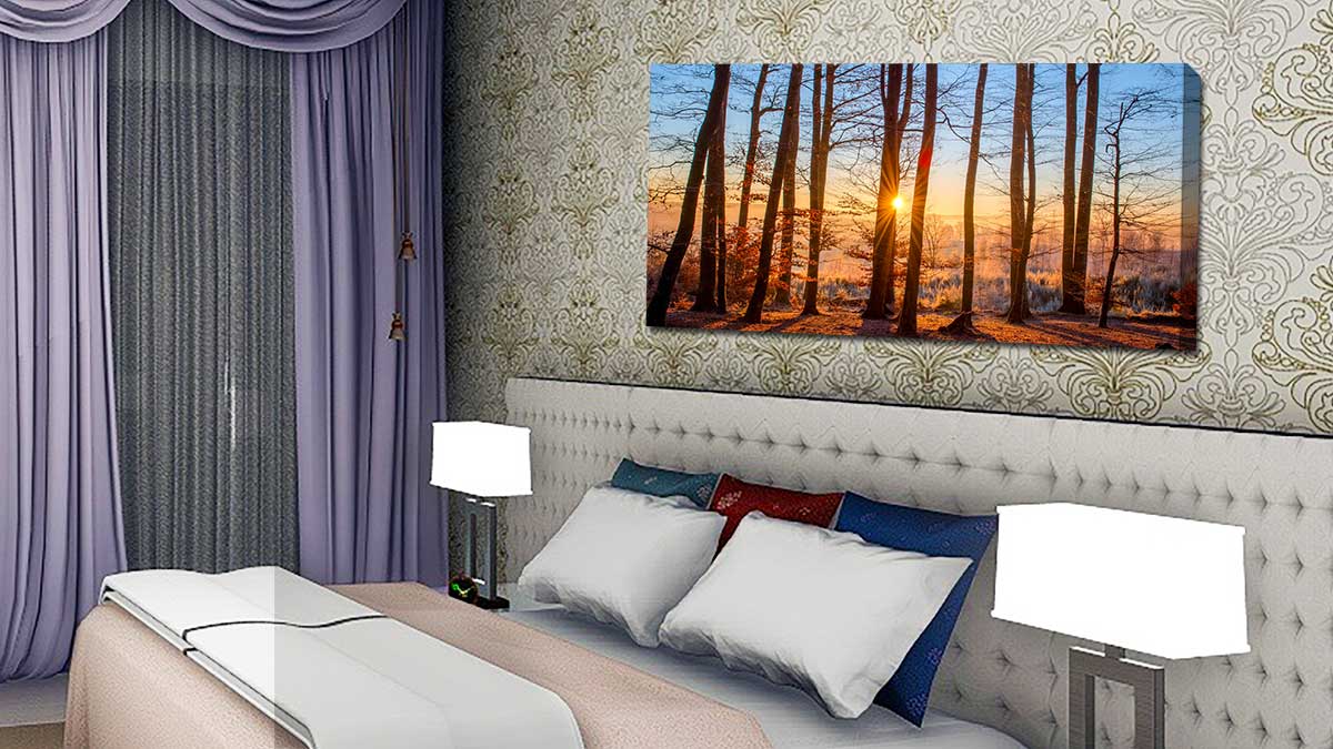 Panoramic canvas print of trees at sunset hung above a bed