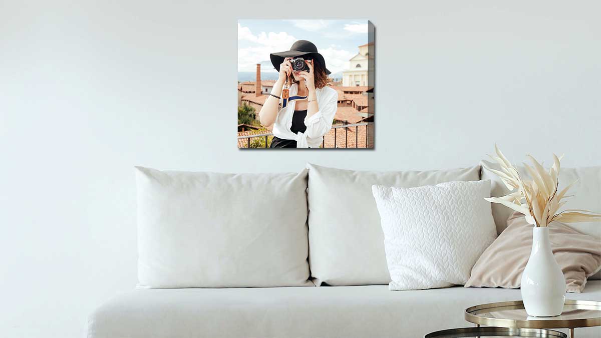 Canvas print featuring a picture of a woman taking a photo with her camera hanging on a wall above a white sofa.